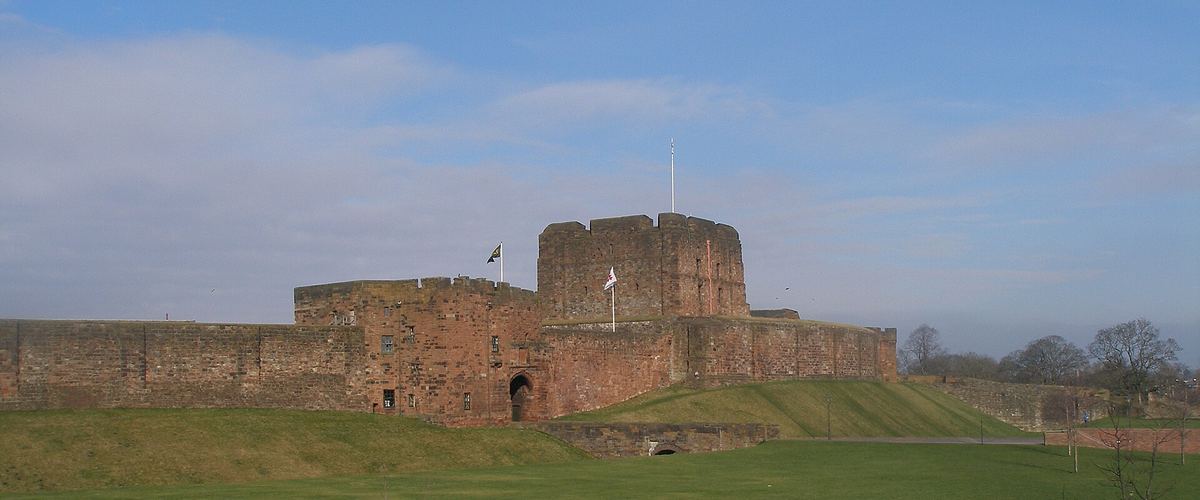 Carlisle Castle's red sandstone keep and curtain wall, seen across the grass on a clear day